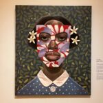 A portrait painting of a woman with a floral mask-like pattern on her face and white flowers in her hair, set against a leafy green background. She wears a blue collared dress with white polka dots.