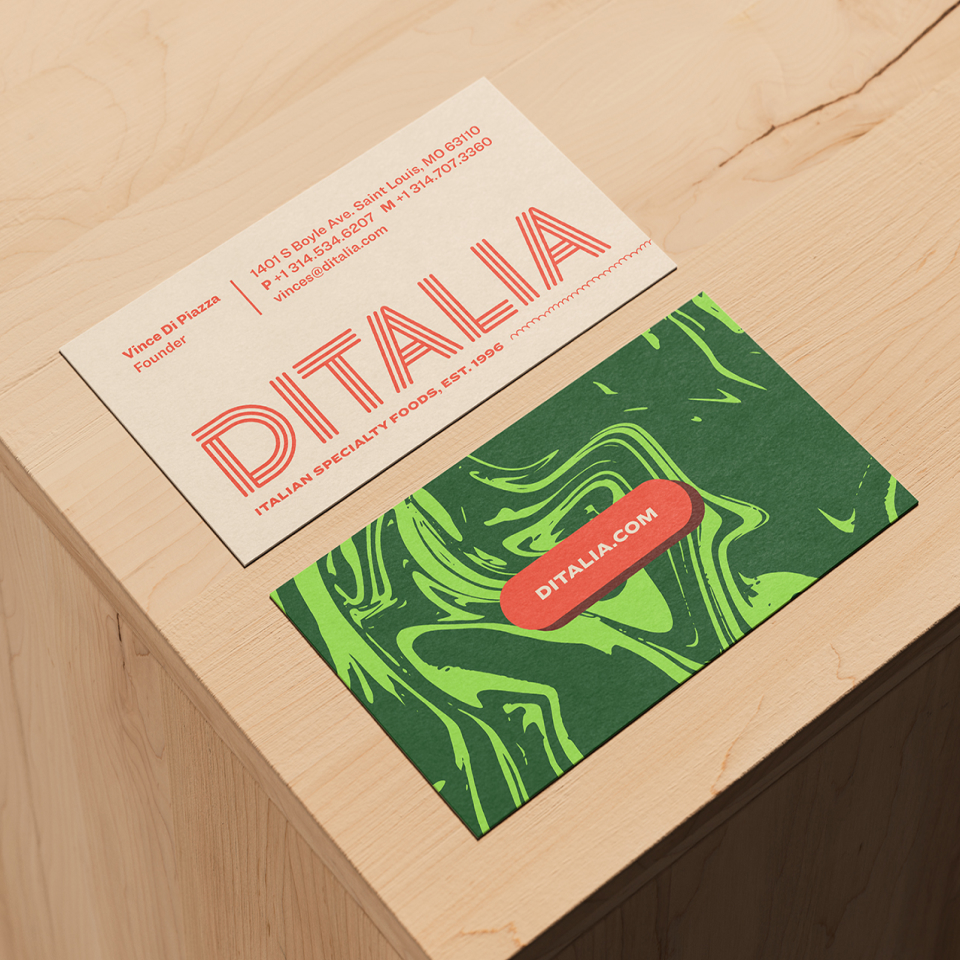 Two business cards on a light wooden surface: one cream card with red text showing contact info for DITALIA, and one green card with a swirling pattern and a red oval containing “DITALIA.COM” in white.