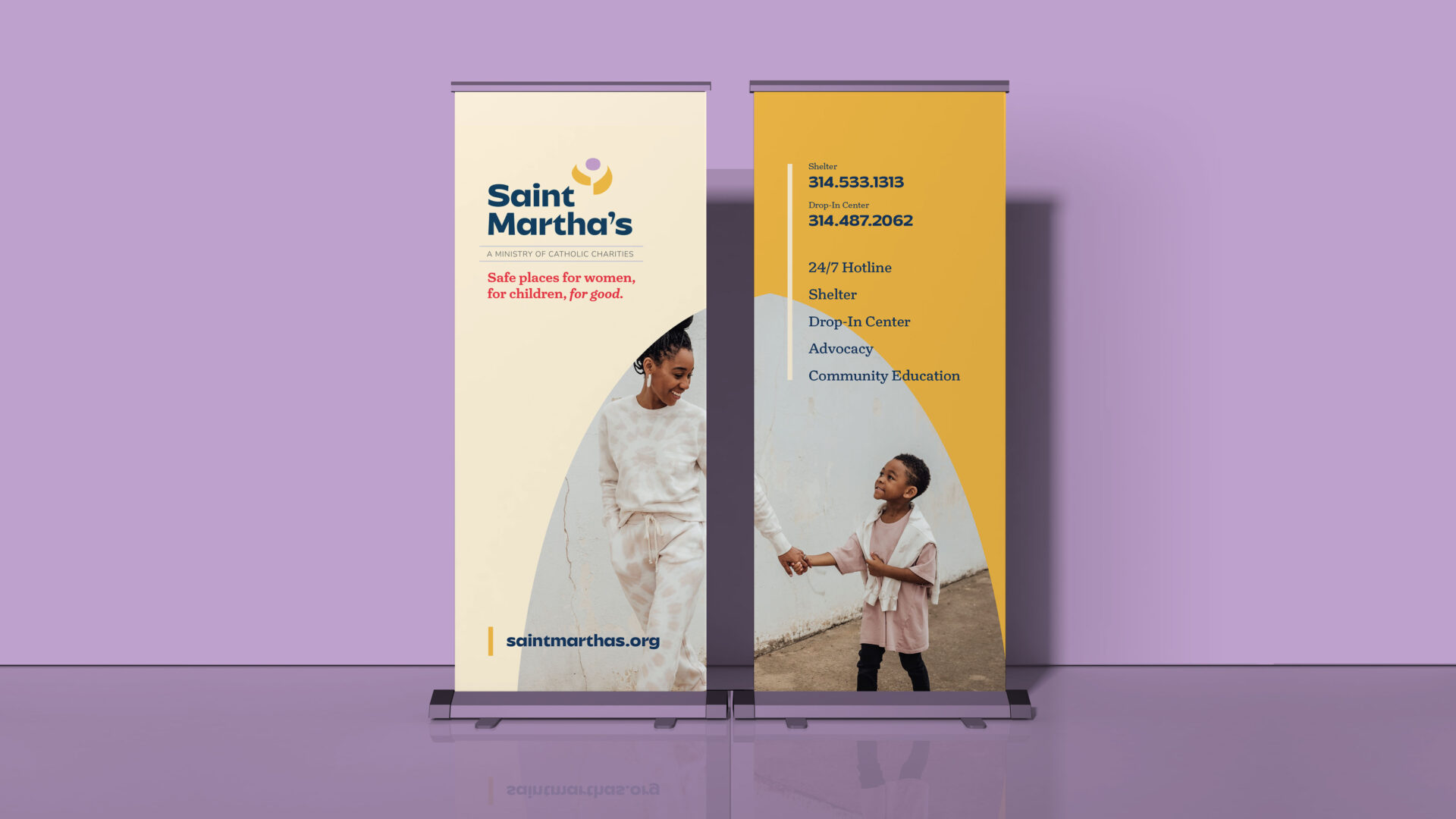 Two standing banners on a purple floor against a lavender wall. The left banner shows Saint Marthas and their tagline, with a photo of a woman and child. The right banner lists contact details and services, with a photo of two children smiling.